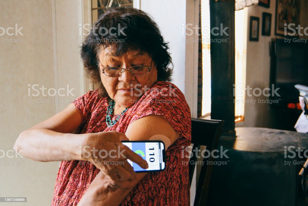 A senior aged Indigenous Navajo woman, checking her blood glucose level with a smartphone application.